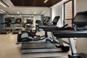Kuntosali, jossa on useita kuntoilulaitteita, kuten juoksumattoja ja crosstrainereita, jotka on järjestetty riveihin.
