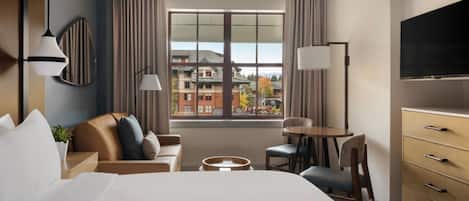 A hotel room with a bed, a desk, a chair, a TV, and a window with curtains.