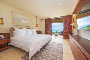 A bedroom with a large bed, a nightstand, a bedside table, a lamp, a painting, a window with a view, and a wooden door. - Condo Las Olas 4BD - Tau Punta Mita (Punta de Mita)