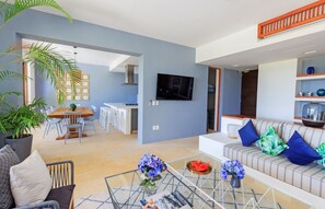 A modern living room with a sofa, coffee table, and a dining area with chairs and a table. - Condo Terramar 4BD - Terrazas Punta Mita (Punta de Mita)