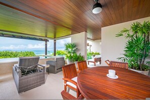 A covered outdoor dining area with a wooden table and chairs, surrounded by potted plants and overlooking a scenic view. - Condo Balboa 3BD - Tau Punta Mita (Punta de Mita)
