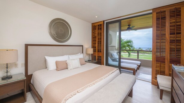 Un dormitorio con una cama grande, una mesita de noche, una lámpara y vistas al exterior a través de una puerta corredera.