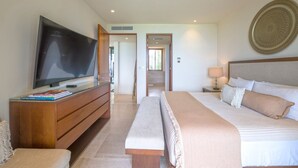 Una habitación de hotel con una cama grande, un televisor sobre un mueble de madera, una mesita de noche con lámpara y un adorno en la pared.