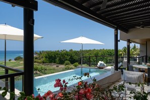 A poolside area with a view of the ocean, surrounded by greenery and equipped with umbrellas. - Condo Piscis 3BD - Marietas Punta Mita (Punta de Mita)
