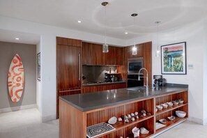 A modern kitchen with wooden cabinetry, stainless steel appliances, and a central island with a built-in sink. - Condo Piscis 3BD - Marietas Punta Mita (Punta de Mita)