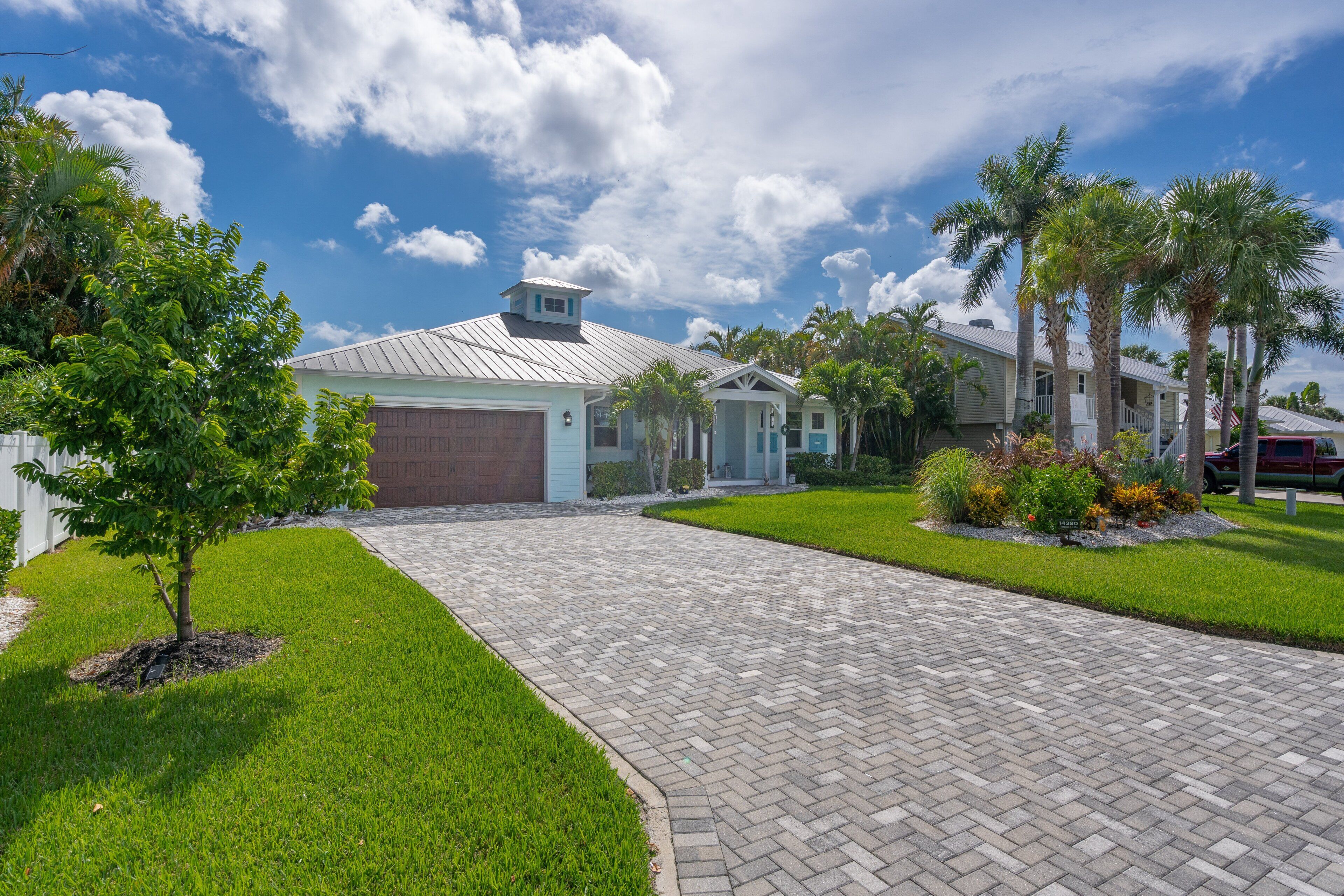 A residential driveway leading to a house with a garage, surrounded by well-maintained lawns and palm trees.