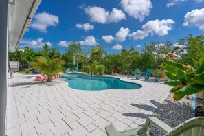 A swimming pool with a curved design, surrounded by a paved patio with chairs and potted plants. - Coastal Bokeelia Retreat | Zero-Entry Pool + Boat Trailer Parking Near Pineland Marina (Bokeelia)