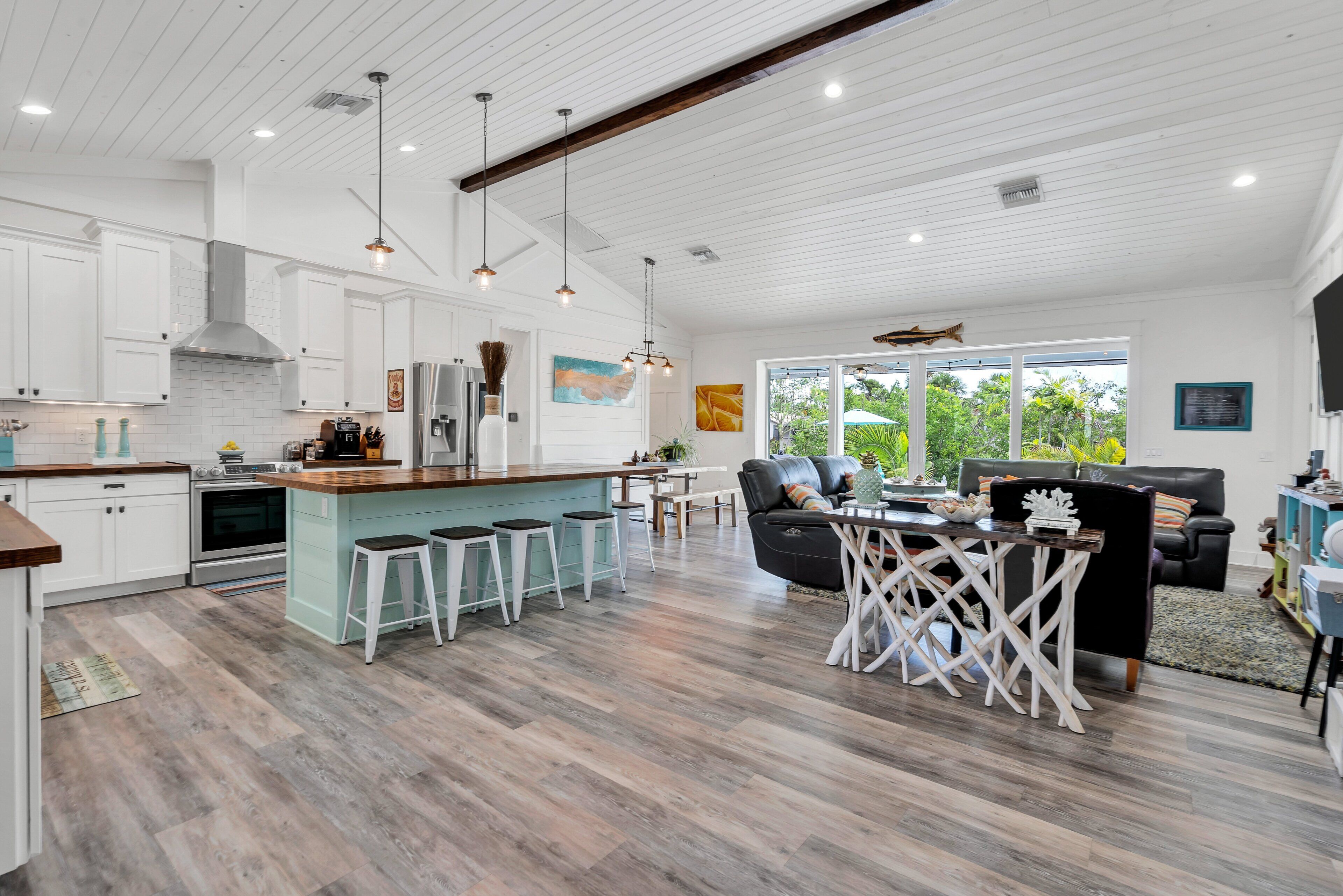 A spacious kitchen with white cabinetry, a central island with bar stools, and a dining area with a black leather sofa and a wooden table.