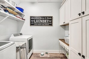 A laundry room with a washing machine, dryer, and a sign indicating it's open 24 hours. - Coastal Bokeelia Retreat | Zero-Entry Pool + Boat Trailer Parking Near Pineland Marina (Bokeelia)
