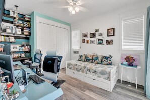 A well-organized bedroom with a desk, computer, chair, bed with decorative pillows, wall-mounted pictures, and a small side table with a vase. - Coastal Bokeelia Retreat | Zero-Entry Pool + Boat Trailer Parking Near Pineland Marina (Bokeelia)