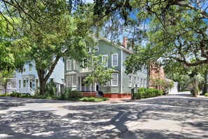 A two-story house with a porch, surrounded by trees and a clear sky. - Bright Modern Retreat in Savannah's Historic District | Heated Pool Access (Savannah)