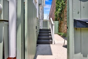 A narrow alleyway with a set of stairs leading to a gated entrance, flanked by buildings with white siding and a brick wall. - Bright Modern Retreat in Savannah's Historic District | Heated Pool Access (Savannah)