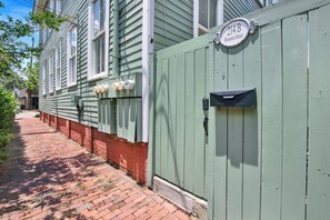 A narrow brick pathway leading to a green wooden building with a mailbox and utility boxes. - Bright Modern Retreat in Savannah's Historic District | Heated Pool Access (Savannah)