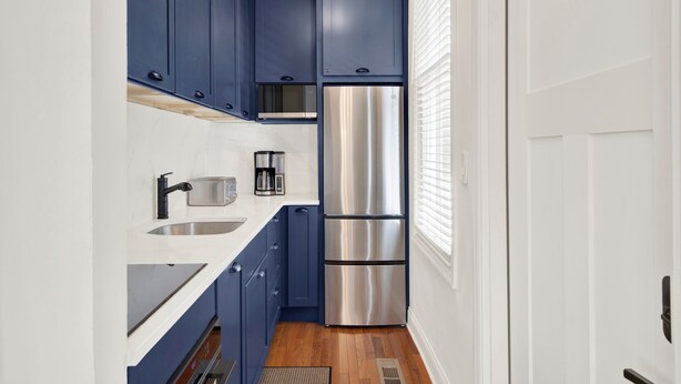 Eine kleine Küche mit blauen Schränken, einem Edelstahlkühlschrank und einem eingebauten Backofen.