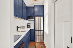 A compact kitchen with blue cabinets, a stainless steel refrigerator, and a built-in oven. - Bright Modern Retreat in Savannah's Historic District | Heated Pool Access (Savannah)