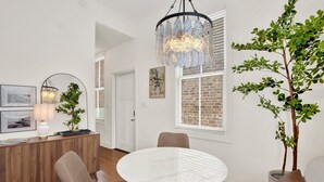 Ein modernes Wohnzimmer mit einem runden weißen Tisch, zwei braunen Stühlen, einer Holzkommode und einem Blumentopf.