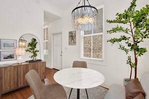 A modern living room with a round white table, two brown chairs, a wooden cabinet, and a potted plant. - Bright Modern Retreat in Savannah's Historic District | Heated Pool Access (Savannah)