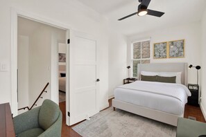 A bedroom with a bed, a nightstand, a lamp, a ceiling fan, and a door leading to another room. - Bright Modern Retreat in Savannah's Historic District | Heated Pool Access (Savannah)