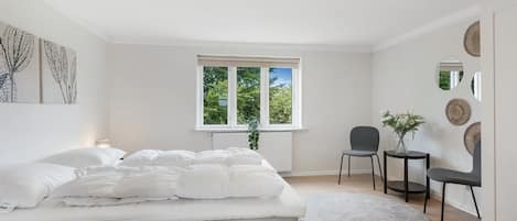 A bedroom with a bed, a chair, a small table, a window, and wall art.