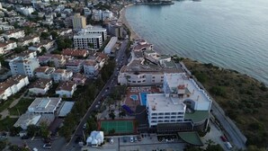 An aerial view of a coastal city with buildings, a beach, and a road. - Ada Newday Resort Hotel & Spa (Kuşadası)