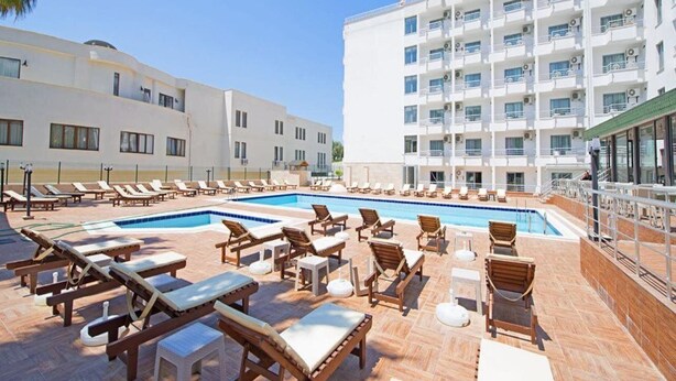 A pool area with sun loungers and a building with multiple balconies. - Ada Newday Resort Hotel & Spa (Kuşadası)