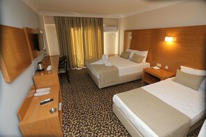 Una habitació d'hotel amb dos llits, una taula amb cadira, una televisió i una finestra amb cortines.