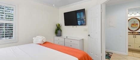 Habitación de hotel con cama, televisor, escritorio y baño visible a través de una puerta abierta.