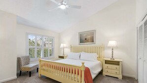 A bedroom with a bed, two bedside tables, a chair, a window with blinds, a ceiling fan, and a painting on the wall. - Sailmaker Gated Complex: Near Pool & Beach (Fernandina Beach)