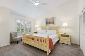 A bedroom with a bed, two bedside tables, a chair, a window with blinds, a ceiling fan, and a painting on the wall. - Sailmaker Gated Complex: Near Pool & Beach (Fernandina Beach)