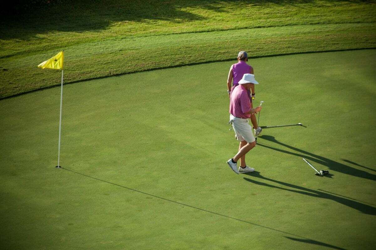 A golf course with a flagstick and a golfer in motion.