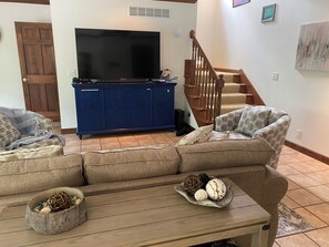 A living room with a large flat-screen TV, a blue entertainment unit, a staircase, and a beige sofa.