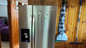 A stainless steel refrigerator in a kitchen with wooden cabinets and a tiled floor.