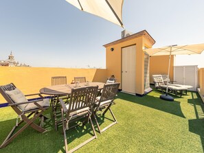 An outdoor patio with a table and chairs, a small building, and a view of a distant building. - Giralda Views Atico Duplex con terraza privada (Sevilla.)