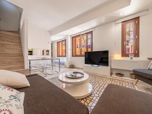 A modern living room with a sofa, a coffee table, a TV, and a staircase. - Giralda Views Atico Duplex con terraza privada (Sevilla.)