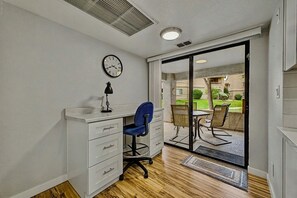 Ein Zimmer mit Schreibtisch, Stuhl und Blick auf einen Innenhof durch eine Schiebetür.