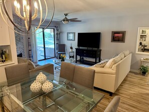 A modern living room with a glass dining table, sofas, a TV, and a ceiling fan. - Cozy 2-bedroom condo in nice Scottsdale with AC for relaxing stays (Scottsdale)