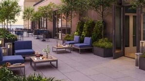 An outdoor seating area with tables and chairs, surrounded by greenery and a building facade. - Landing Amazing Studio, Game Room, Gym (New Rochelle)