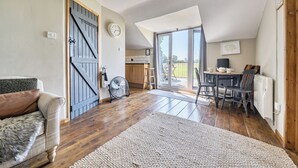A spacious room with a wooden floor, a large window, a dining area, and a cozy seating area. - Hayloft-Sleeps 3-with Enclosed terrace (Dereham)