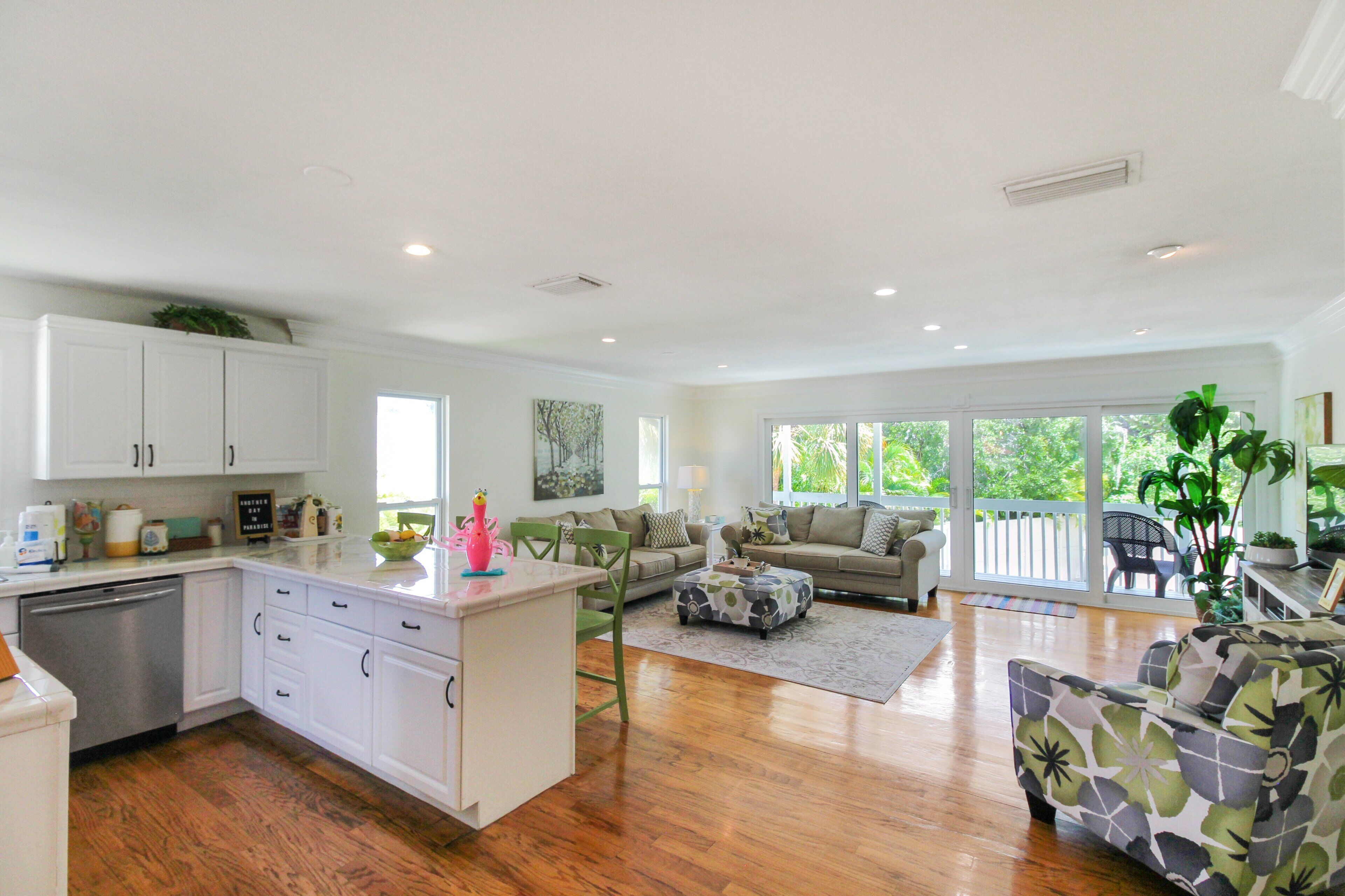 A spacious living area with a kitchen, wooden flooring, and large windows.
