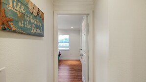 A hallway with a wooden floor leading to a room with a window. A decorative sign is visible on the wall. - Private Siesta Key Pool Home Near Beaches - Siesta Sol (Sarasota)