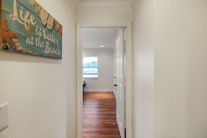 A hallway with a wooden floor leading to a room with a window. A decorative sign is visible on the wall. - Private Siesta Key Pool Home Near Beaches - Siesta Sol (Sarasota)