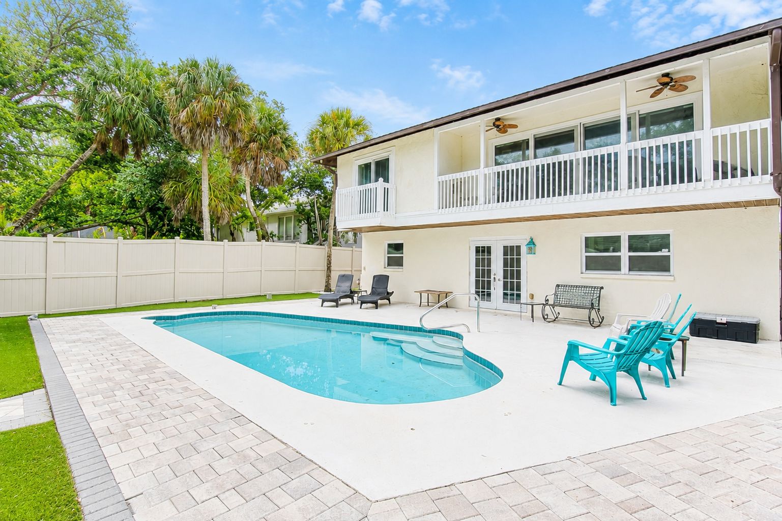 A two-story house with a swimming pool, outdoor seating, and a white fence.