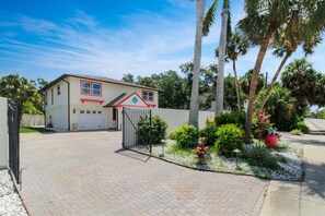 Una casa residenziale con garage, vialetto recintato e un giardino curato con palme e piante fiorite.