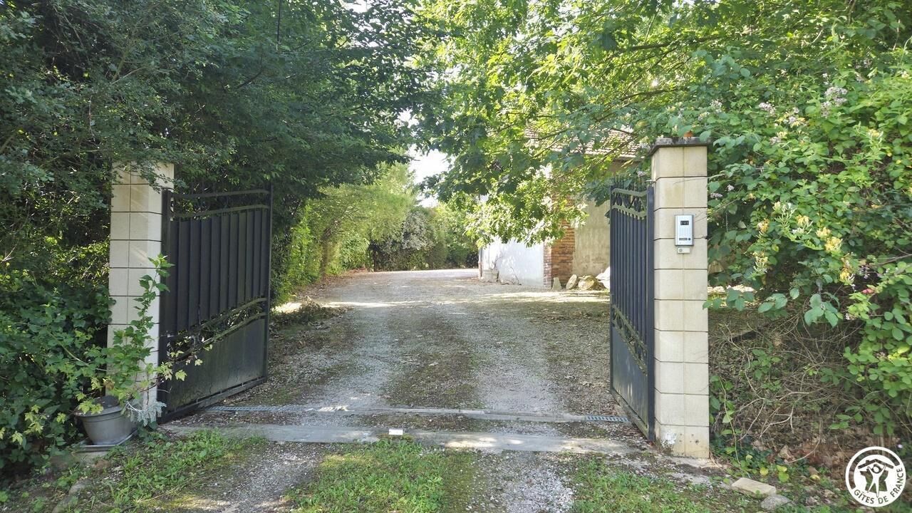 Un camino de entrada con portón que conduce a un edificio con pared exterior blanca.