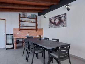 Ein Essbereich mit einem langen Tisch und Stühlen, eine Küche mit Ziegelrückwand und eine Wand mit einem Gemälde von Booten.