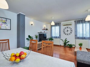 Ein modernes Wohnzimmer mit Essbereich, ausgestattet mit einem Fernseher, Holzmöbeln und Zierpflanzen.