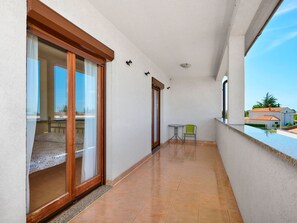 Ein Balkon mit einer Schiebetür, die zu einem Schlafzimmer führt, ein kleiner Tisch mit einem Stuhl und Blick auf eine Wohngegend.
