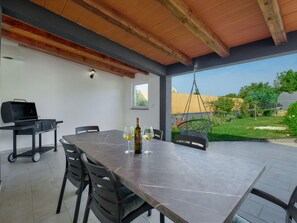 Um pátio externo com mesa, cadeiras, churrasqueira e uma garrafa de vinho.