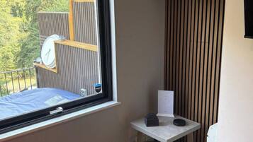 A room with a window, a small table with a clock, and a view of greenery outside.