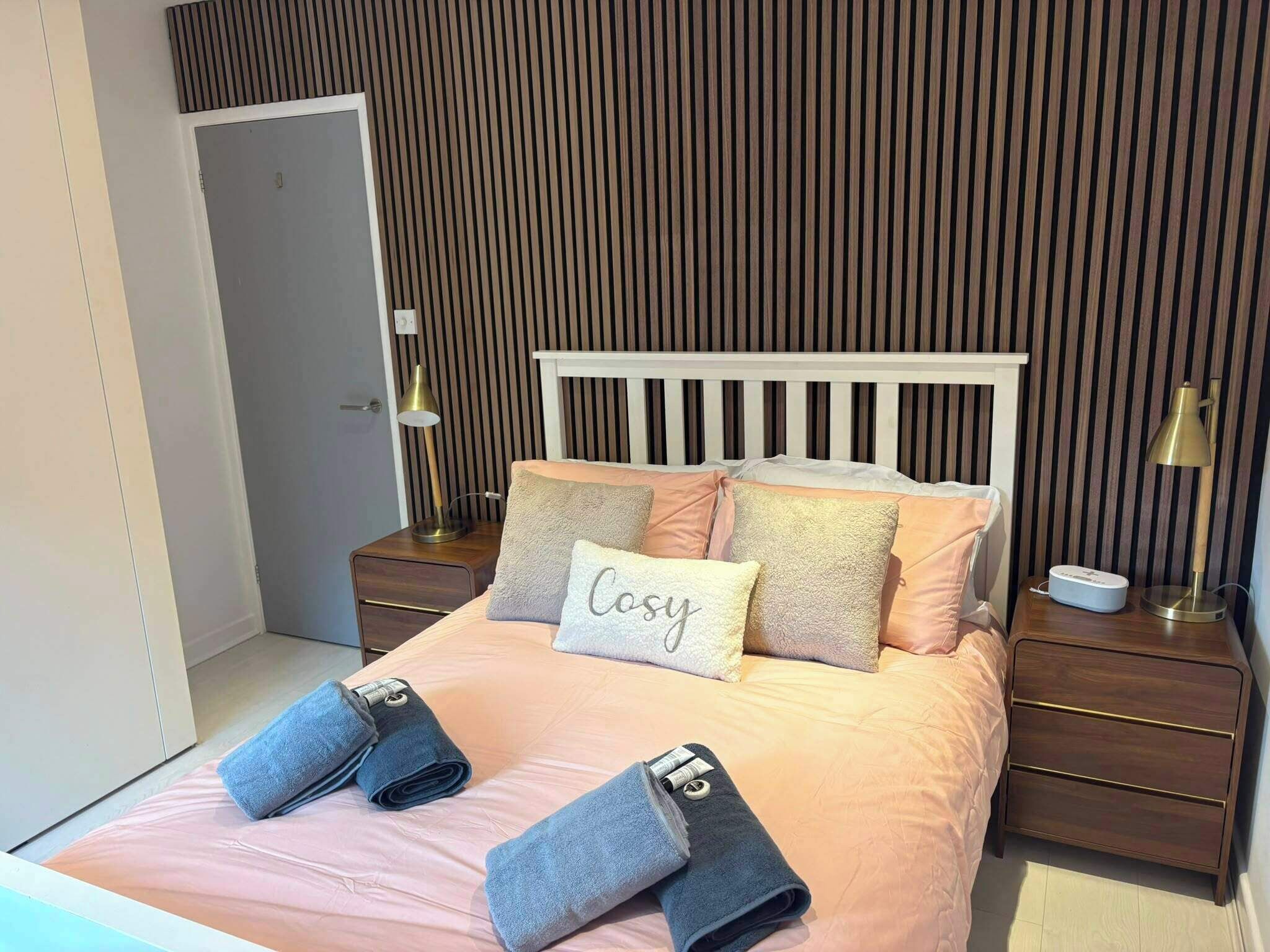 A bedroom with a bed, bedside tables, lamps, and a wall with vertical lines.